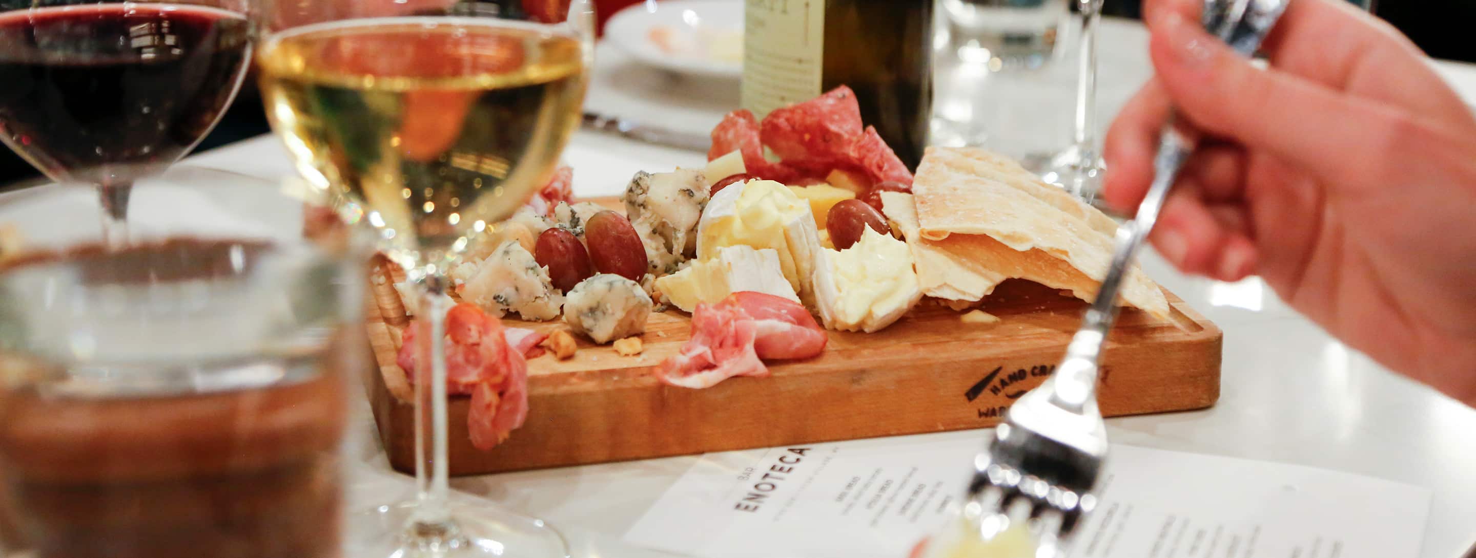 Charcuterie board with various meats and cheeses on a table with wine glasses at Bar Enoteca in Jackson, Wyoming.