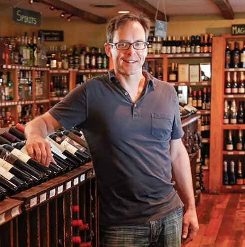 Portrait of Fine Dining Restaurant Group Vice President of Beverage, Neil Loomis, standing next to the wine selection at Bin 22 restaurant in Jackson, Wyoming.